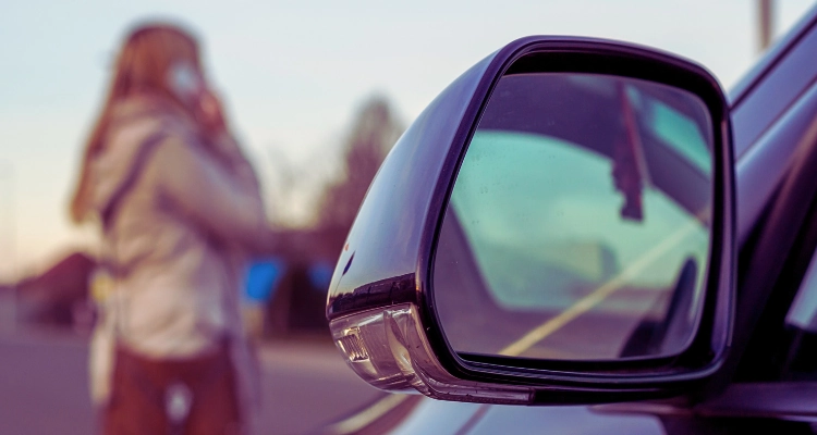 A car side mirror and a worried woman using her smart phone.